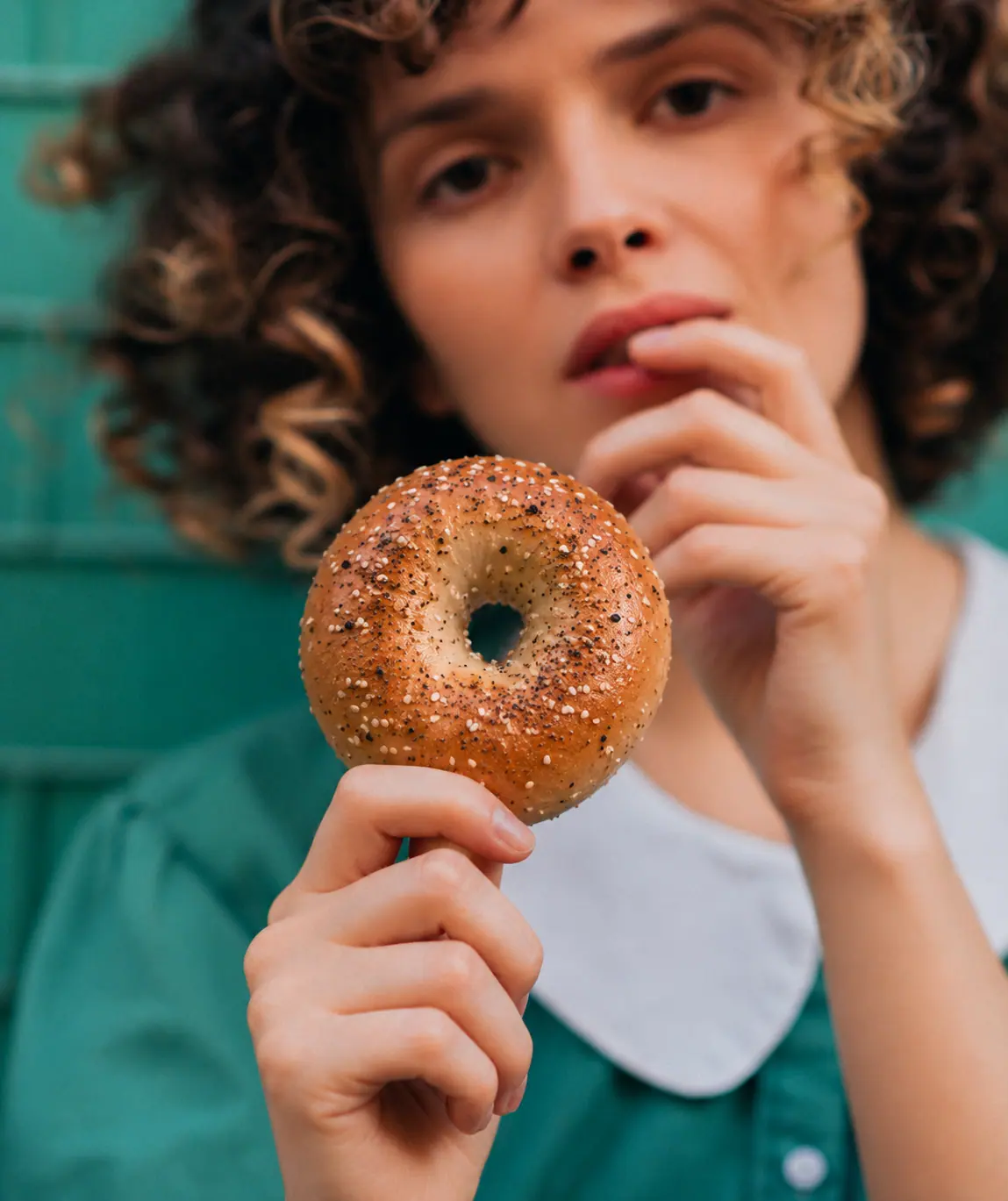 Woman holding an everything bagel against a teal wall